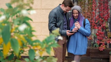 Couple hugging and using a smartphone in the street