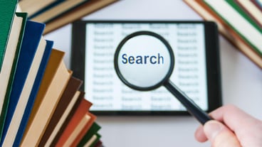 Hand holding a magnifying glass over a tablet surrounded by books search concept