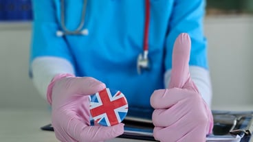 Medical professional displays a round pin with the UK flag and gives a positive thumbs up