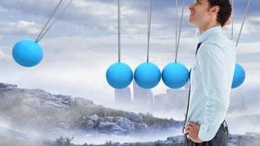 Thinking businessman with hand on head against newtons cradle above city in mountains