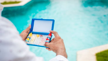 Hand holding Water Test Kit on blurred pool background Hand holding a pool ph and chlorine tester Person holding complete water test kit with blurred pool background