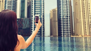 summer, travel, tourism, technology and people concept - close up of sexy young woman taking selfie with smartphone over infinity edge swimming pool in dubai city background