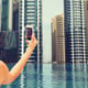 summer, travel, tourism, technology and people concept - close up of sexy young woman taking selfie with smartphone over infinity edge swimming pool in dubai city background