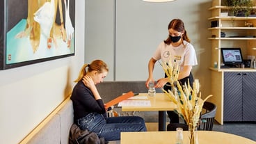 Waitress in mask pours water to woman sitting at table