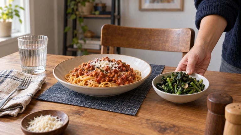 A bowl of greens is placed beside a familiar pasta meal.