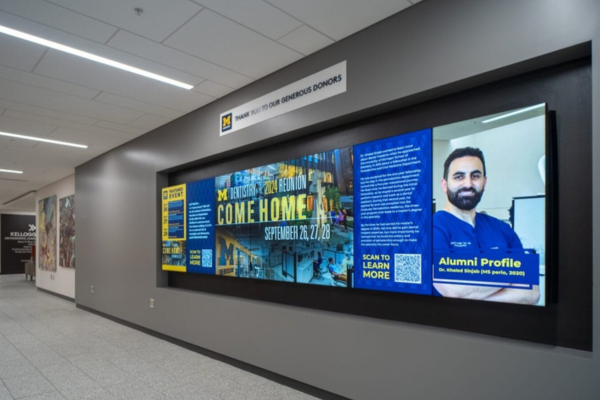 Indoor LED screen displaying alumni profile and event details in a hallway