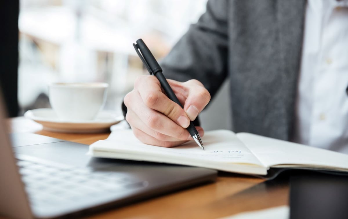 imagem-recortada-de-empresario-sentado-junto-a-mesa-de-cafe-com-computador-portatil-e-escrever-algo