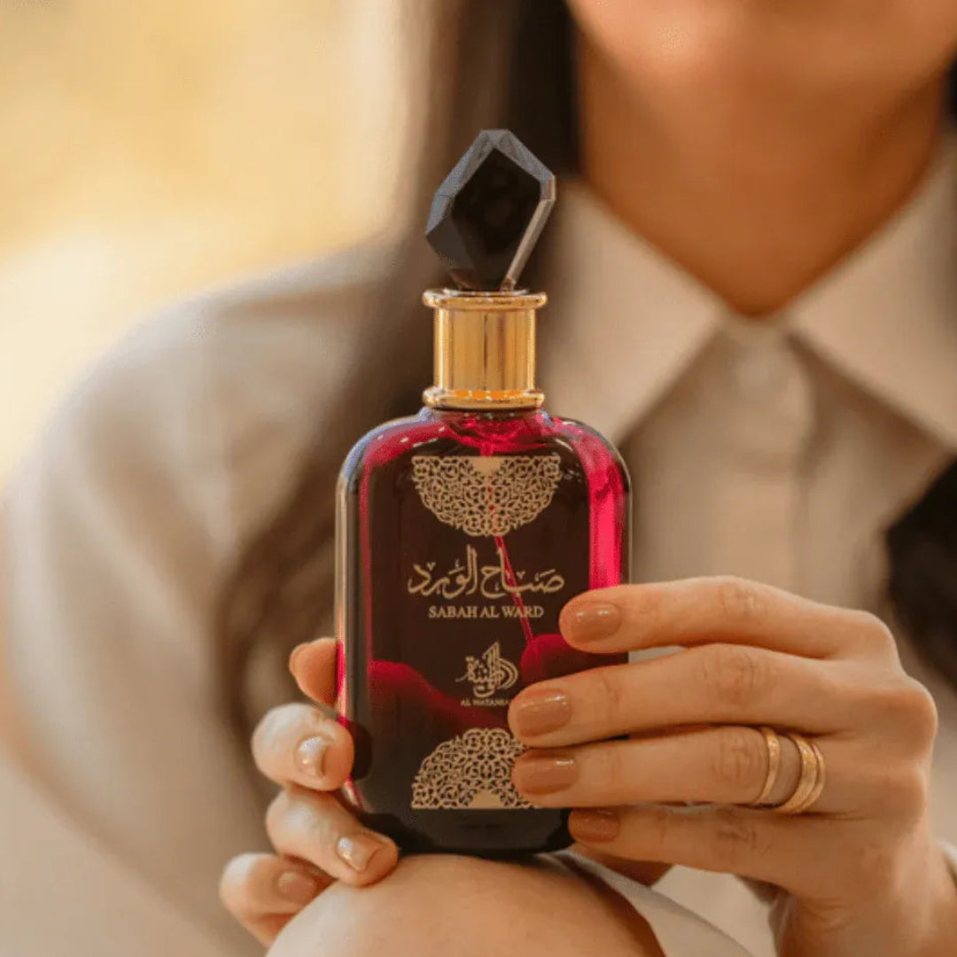 Person holding a red and black perfume bottle with intricate design
