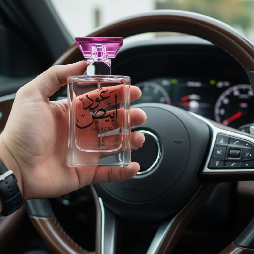 Hand holding a perfume bottle with Arabic text in front of a car dashboard.