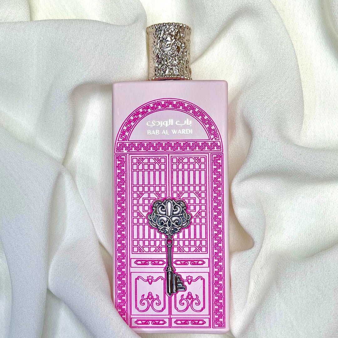 Perfume bottle with pink packaging featuring decorative elements on a white fabric background