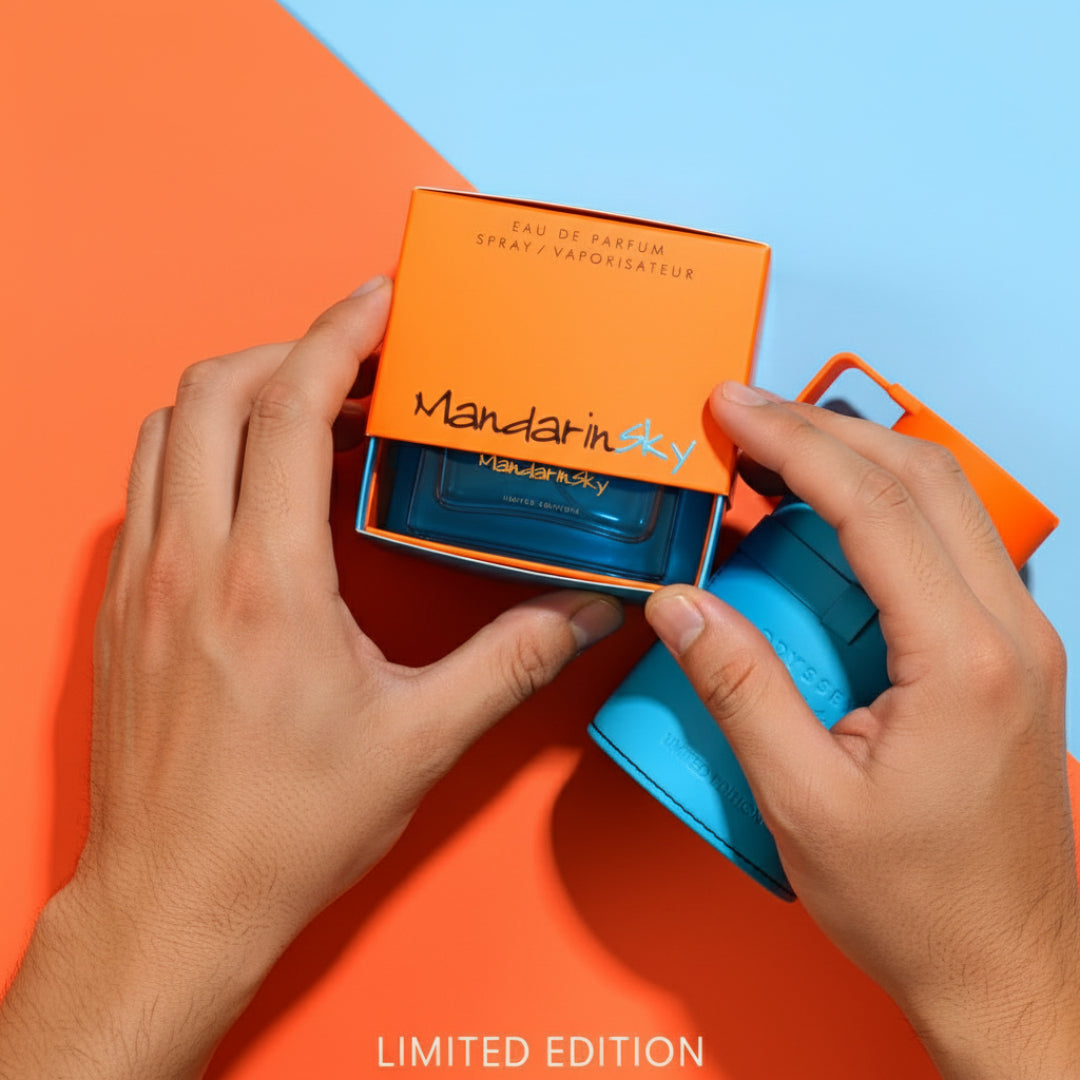 Hands opening a Mandarin Sky perfume bottle with an orange box on a colorful background