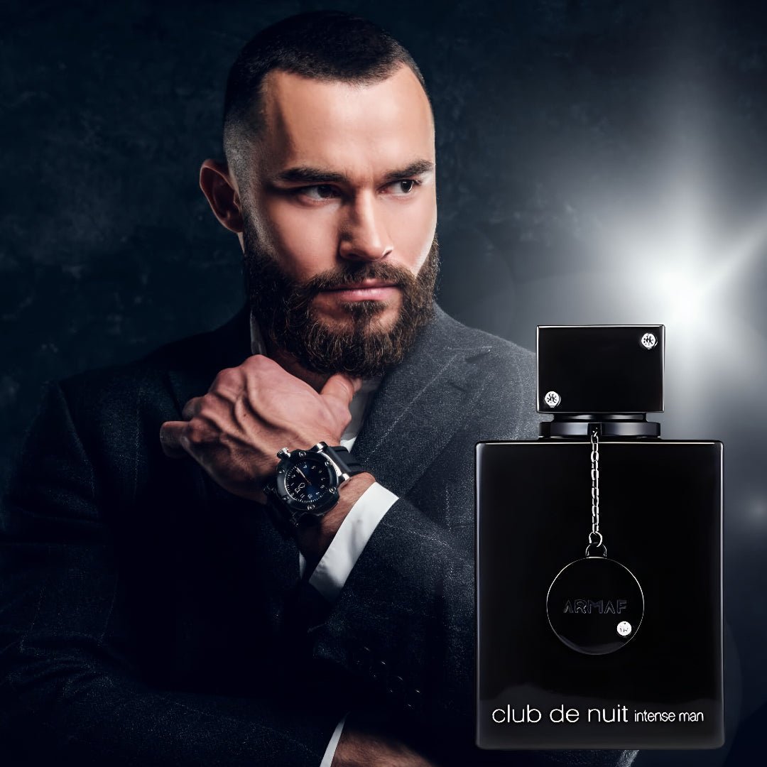 Man in a suit with a beard holding a watch, next to an Armaf 'club de nuit intense man' perfume bottle.