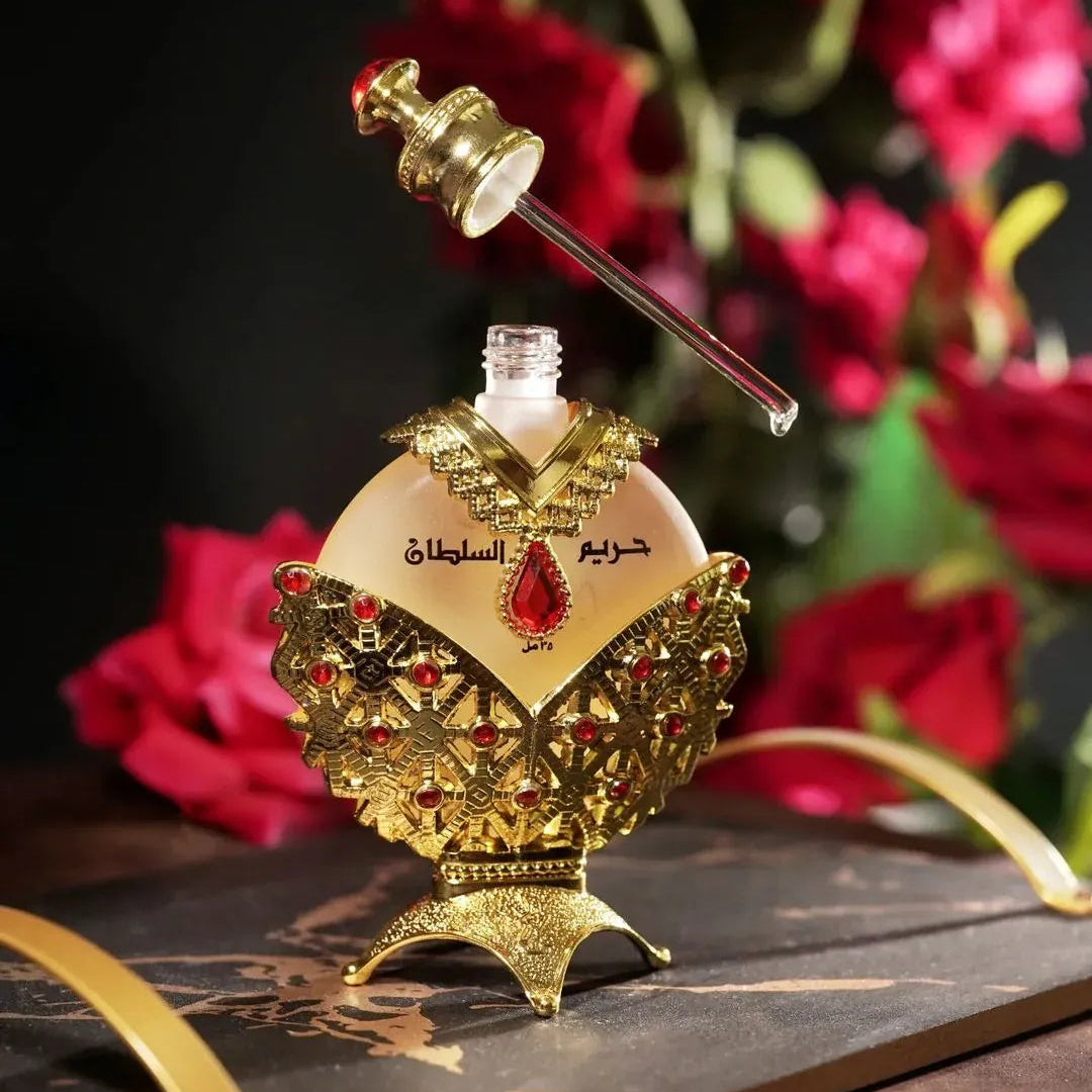 Decorative perfume bottle with gold accents and red gemstones on a dark surface with flowers in the background.