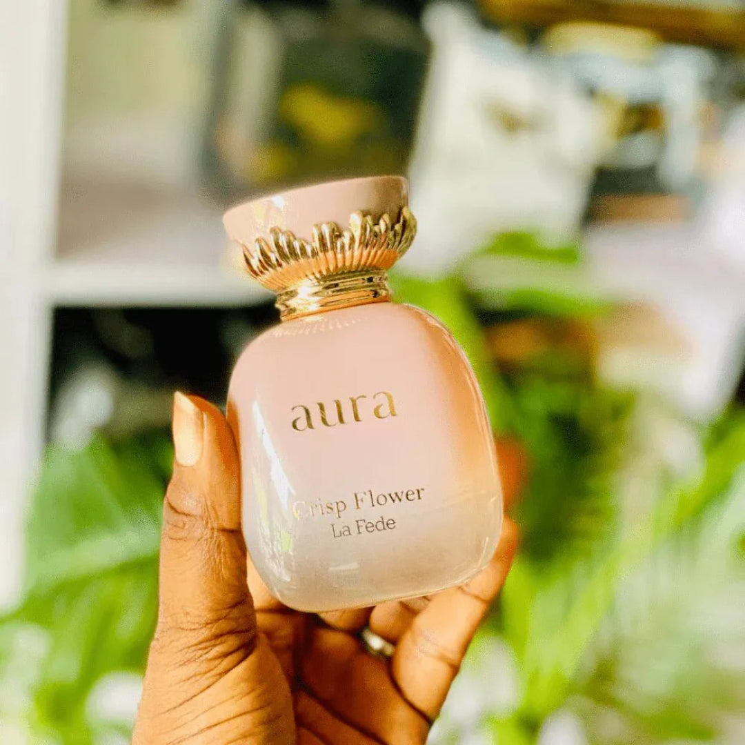 Hand holding a pink 'aura' perfume bottle with a blurred green background