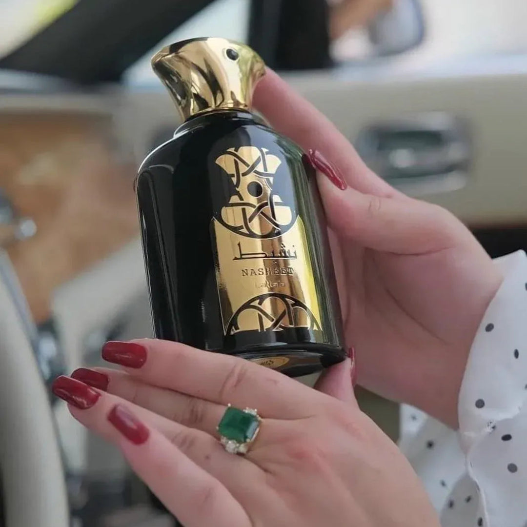 Hand holding a black and gold bottle with 'L'OREAL' branding, inside a car.