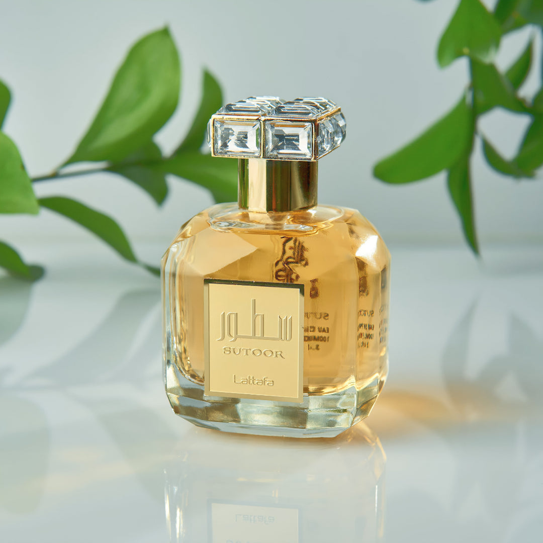 Perfume bottle with decorative cap on a reflective surface with green leaves in the background