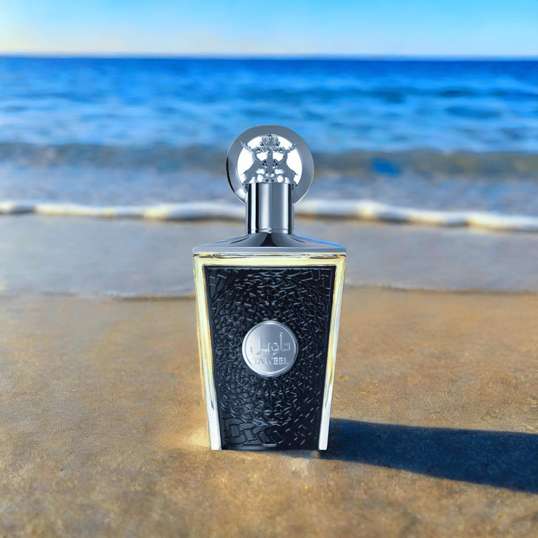 Perfume bottle on a sandy beach with ocean in the background lattafa taweel