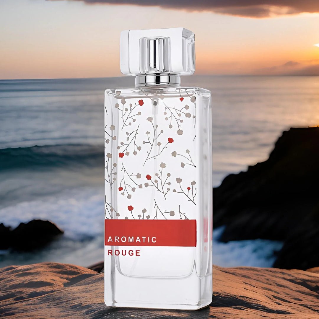 Perfume bottle labeled 'Aromatic Rouge' on a rocky surface with a sunset over water background