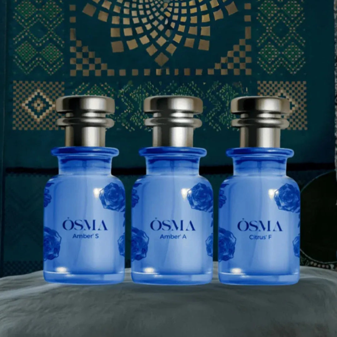 Three blue bottles labeled 'OSMA' on a textured surface with a patterned background.