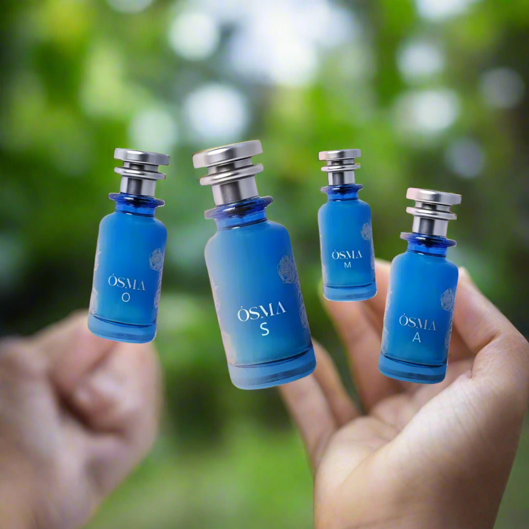 Four blue perfume bottles labeled 'OSMA' against a scenic background with water and sky.