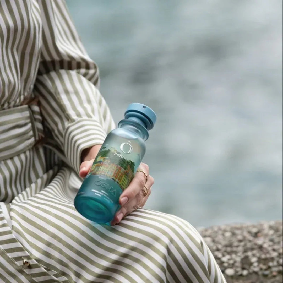 Person holding a blue water bottle with a scenic design against a blurred natural background