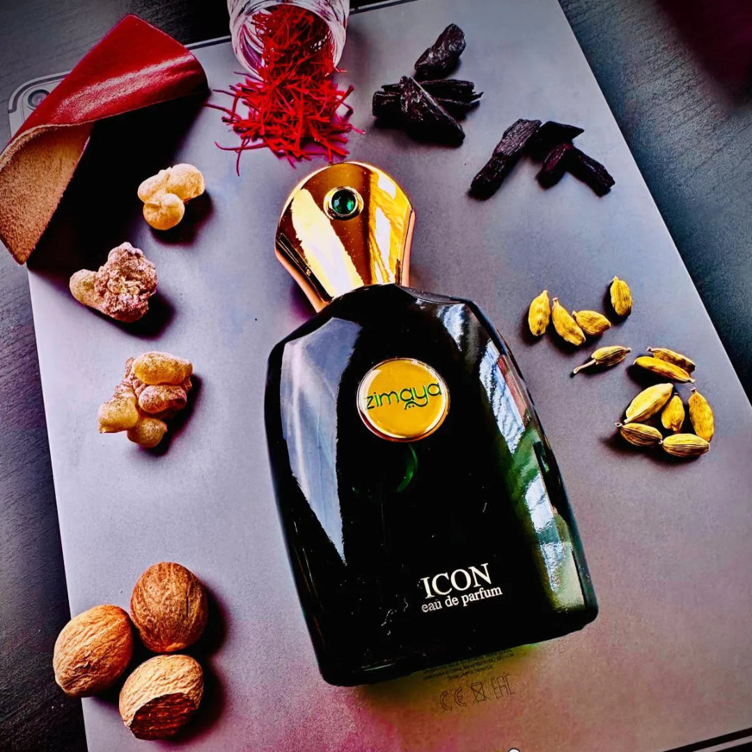 Black perfume bottle with gold cap on a reflective surface surrounded by nuts and leaves