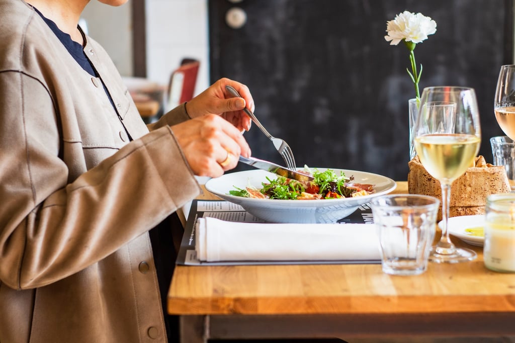 Side view of woman's hands eating a salad at the dinner table