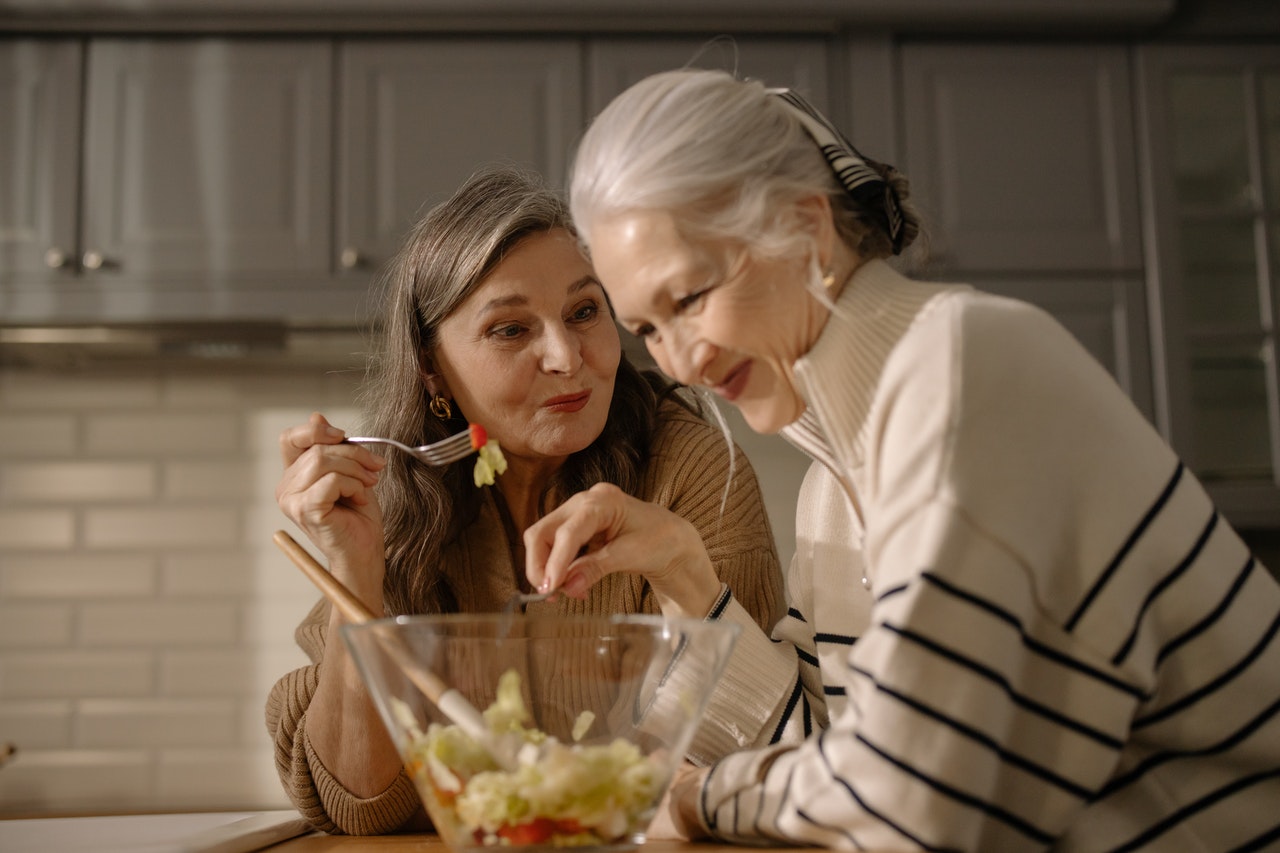 two elderly women eating salad in the kitchen