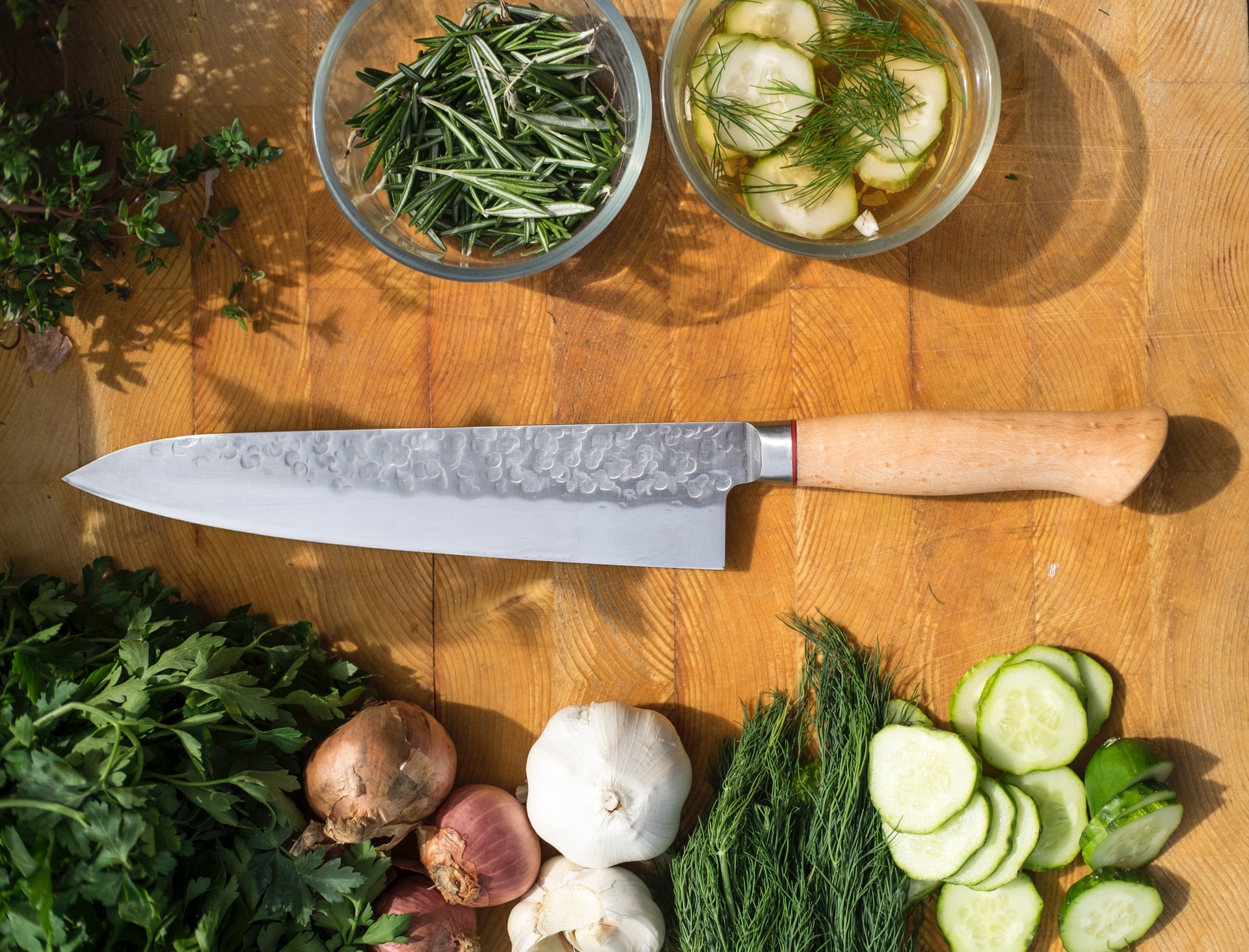 Kitchen knife on a cutting board with herbs, onions, and garlic