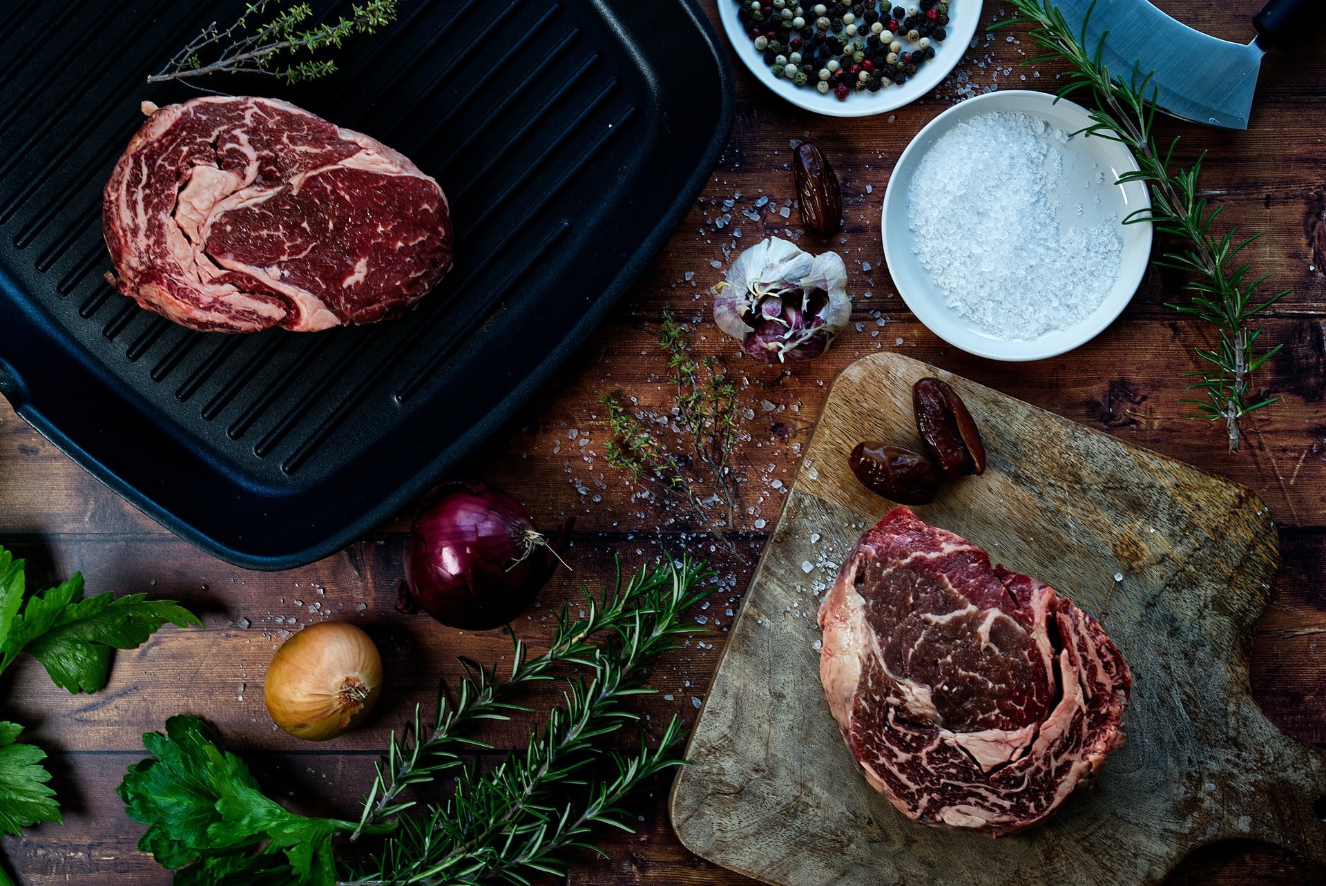 Raw steaks on cutting board with salt, garlic, and onions