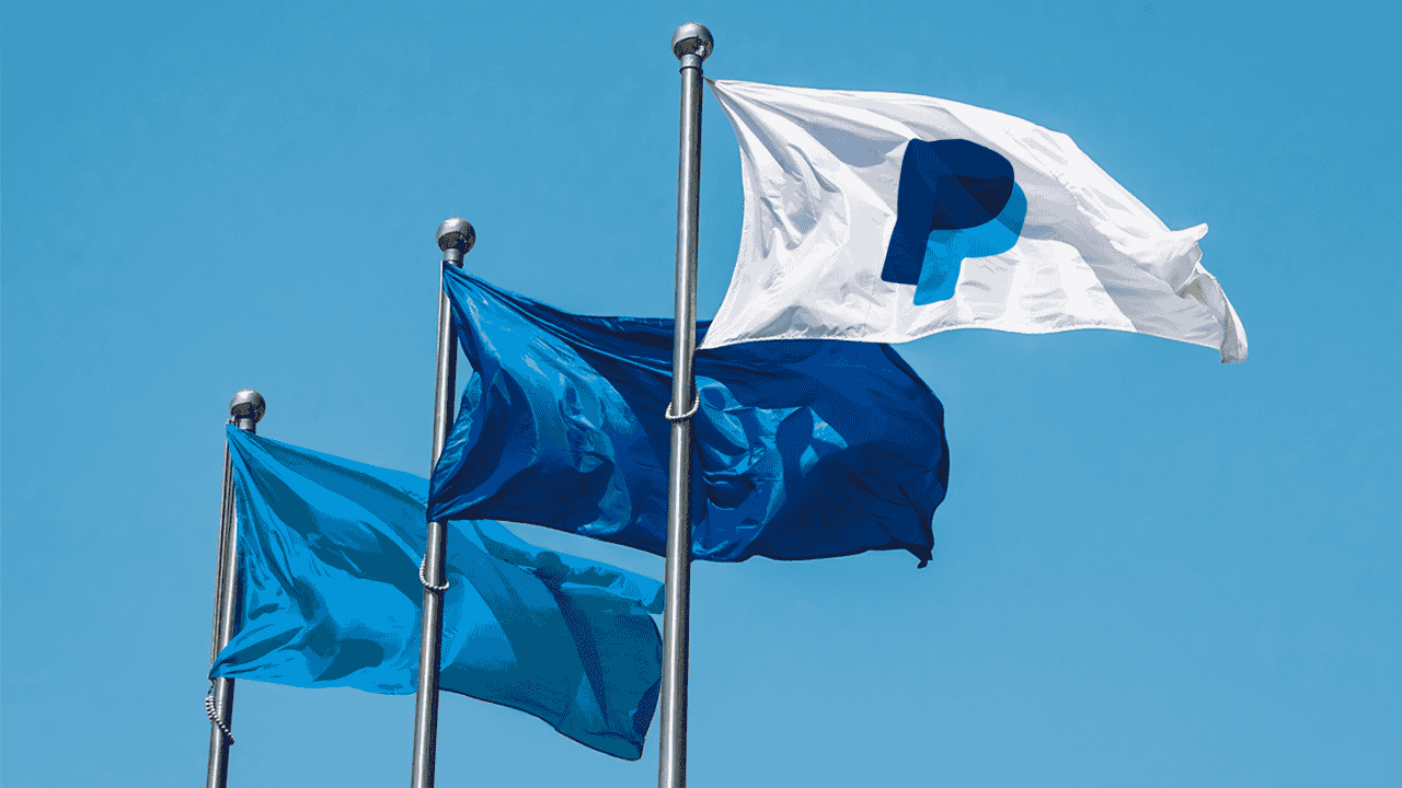 PayPal corporate flags waving against a clear blue sky, including the white flag with the blue PayPal P monogram.