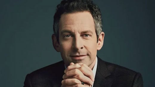 Man with gray hair in dark suit and tie, hands clasped together.
