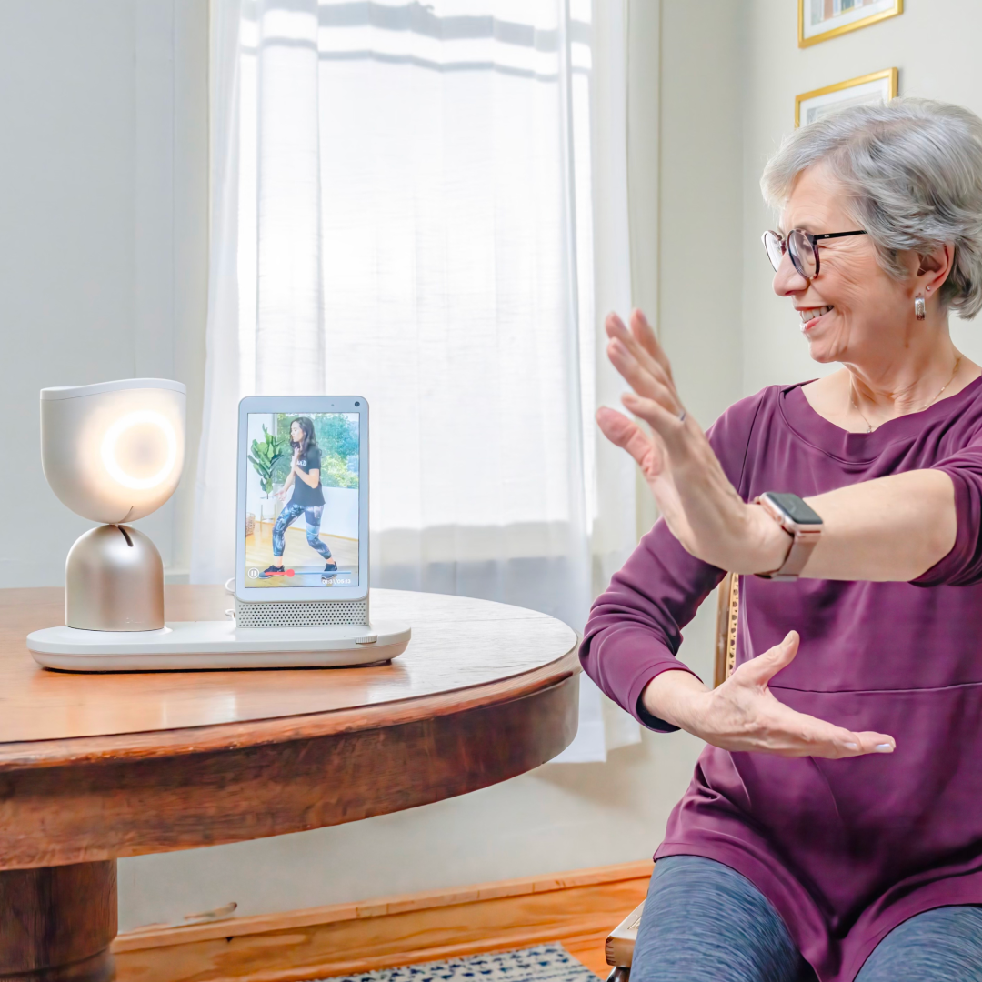 Senior woman with purple top and dark hair gestures at a smart home device