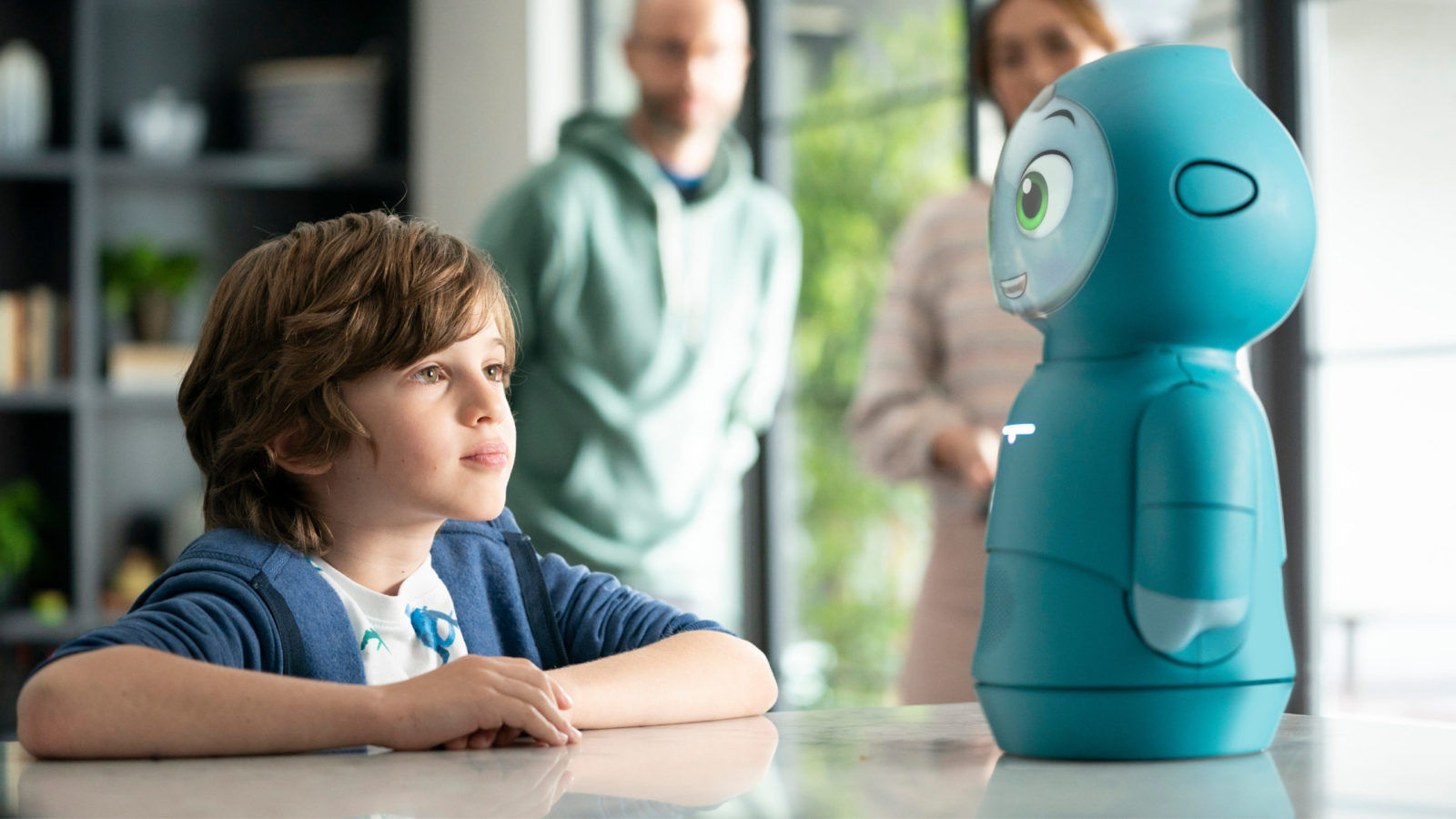 Two people at a table with a blue robot between them