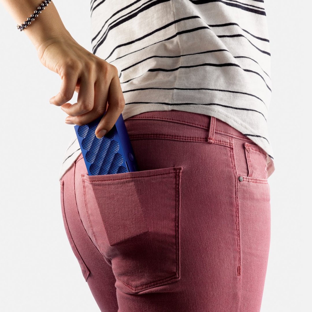 Person holding blue smartphone in hand, wearing pink top and blue jeans