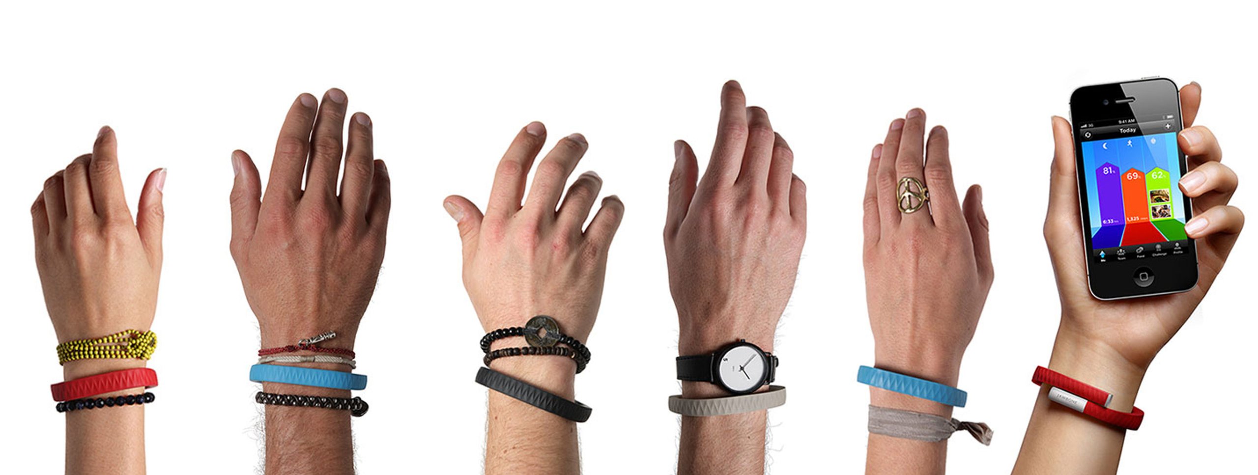 Five wrists wearing Jawbone UP fitness bands in yellow, blue, black, gray, and red colorways styled with friendship bracelets