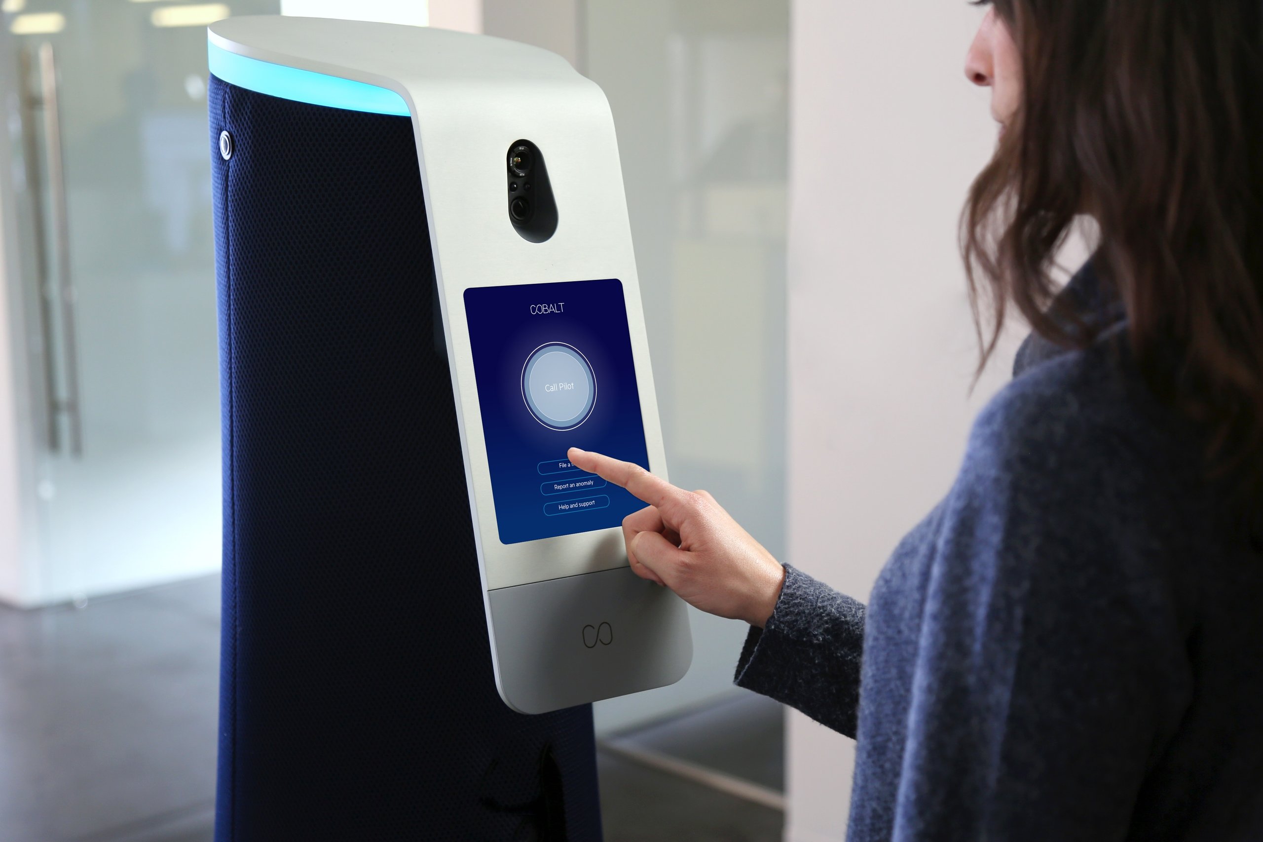 Woman in an office reaching out to tap the Call Pilot button on the Cobalt security robot's touchscreen interface