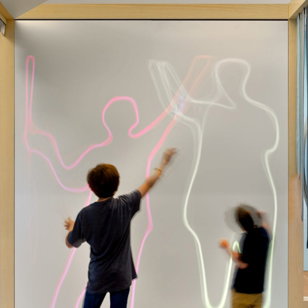 de Youngsters Studio: child and adult interacting with a wall-mounted interactive display showing silhouettes of people
