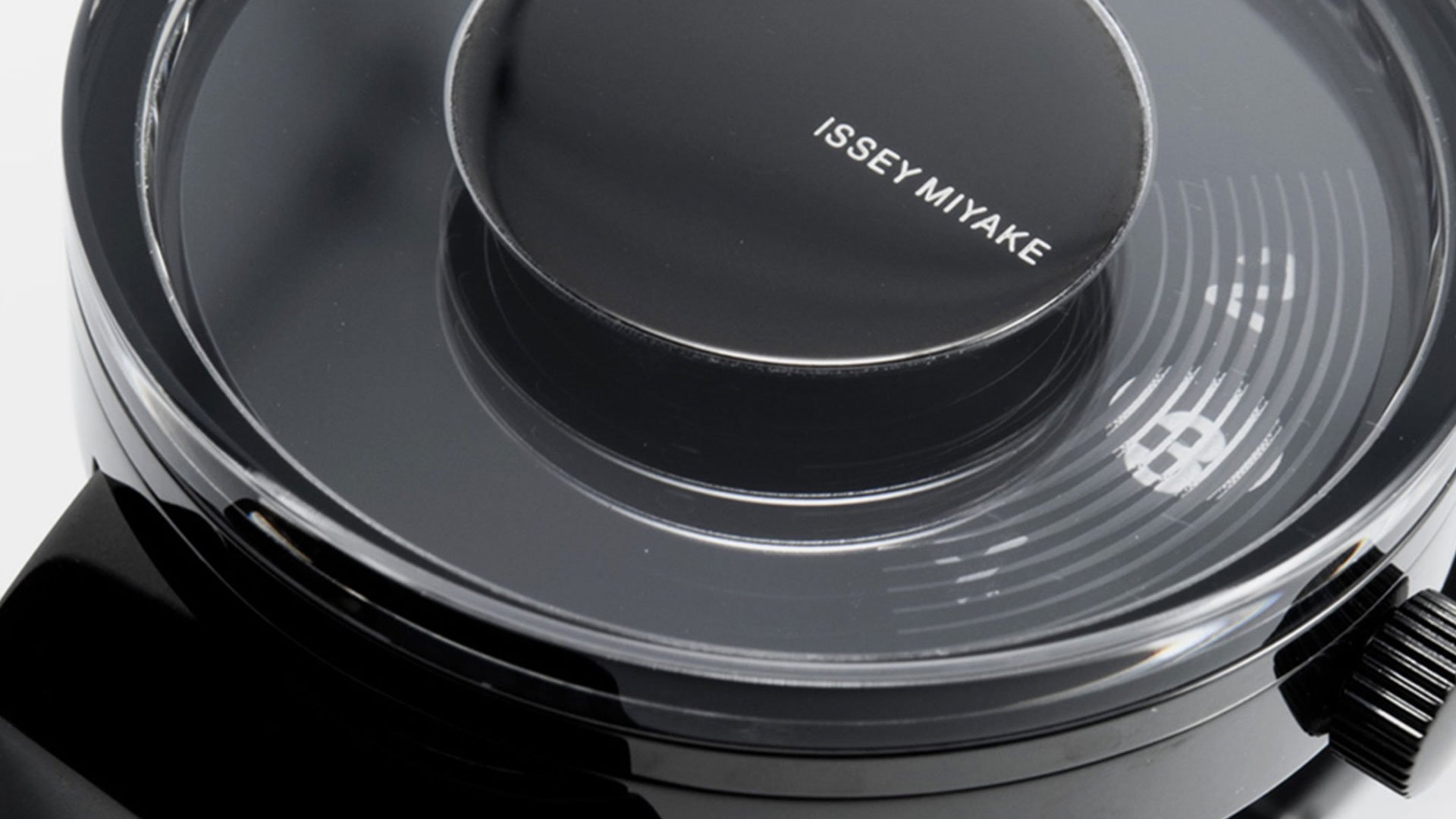 Close-up macro of Issey Miyake VUE watch case showing the floating cylindrical dial with brand wordmark beneath domed sapphir