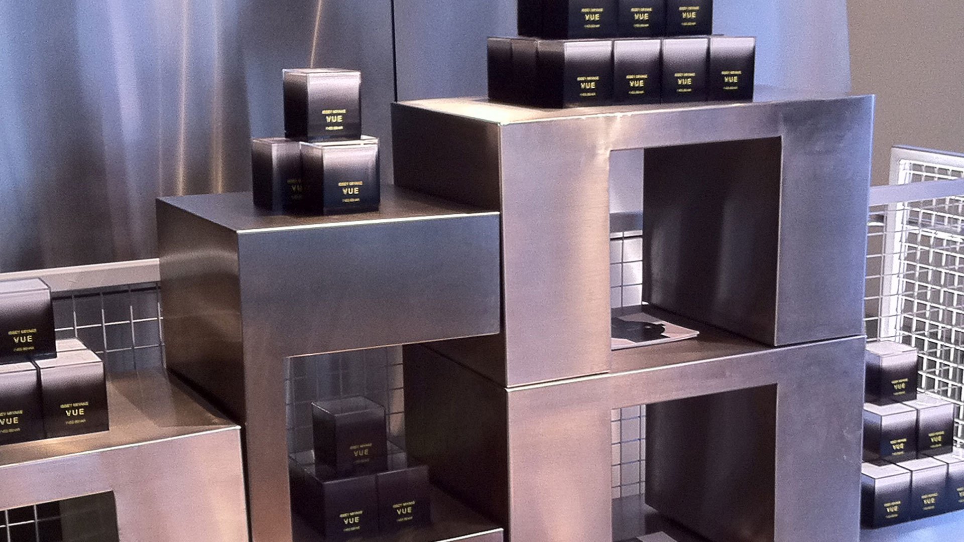 Issey Miyake VUE retail display with stacked geometric brushed-metal pedestals showcasing black VUE watch boxes by Yves Behar