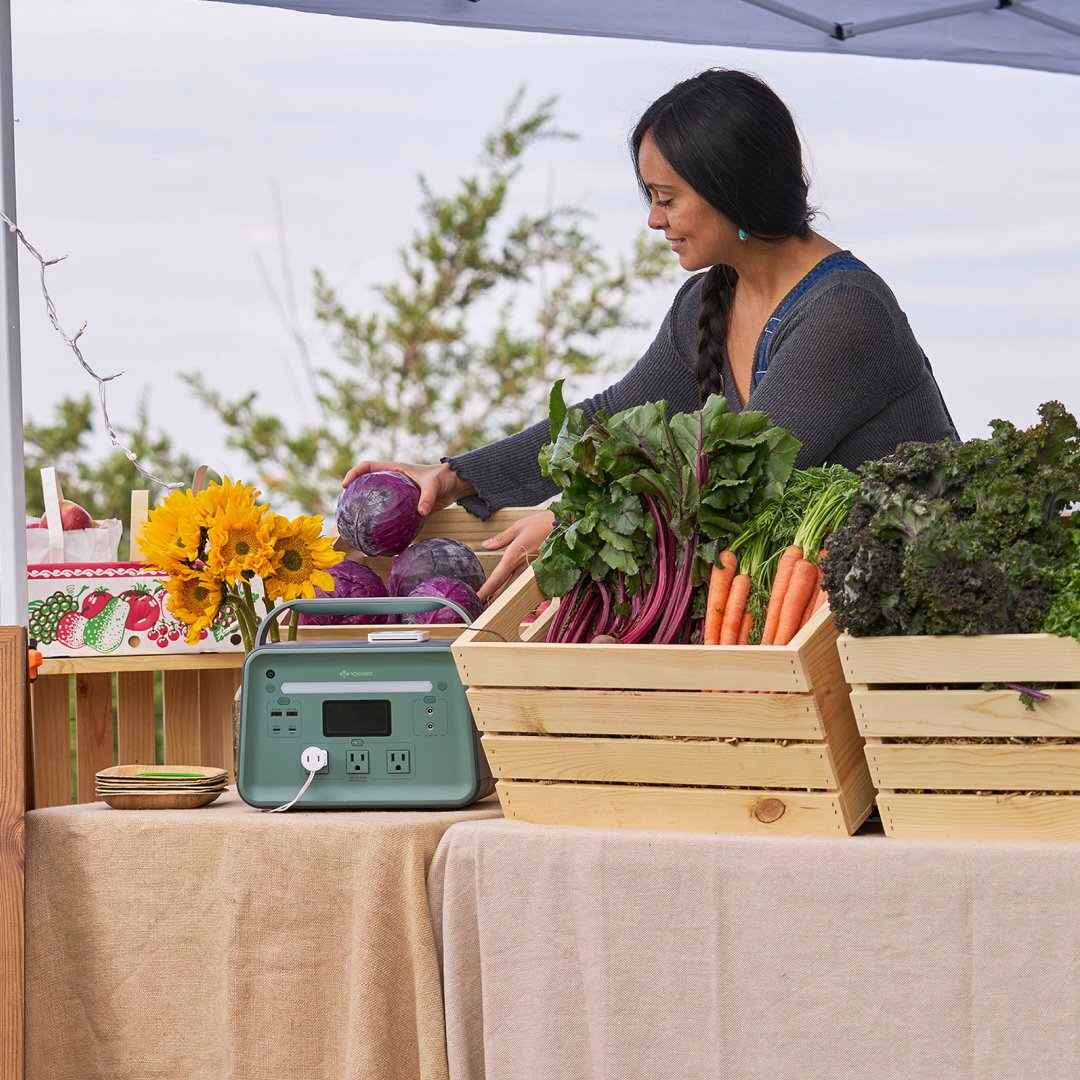 Woman in blue top stands behind table with fresh produce and crates.