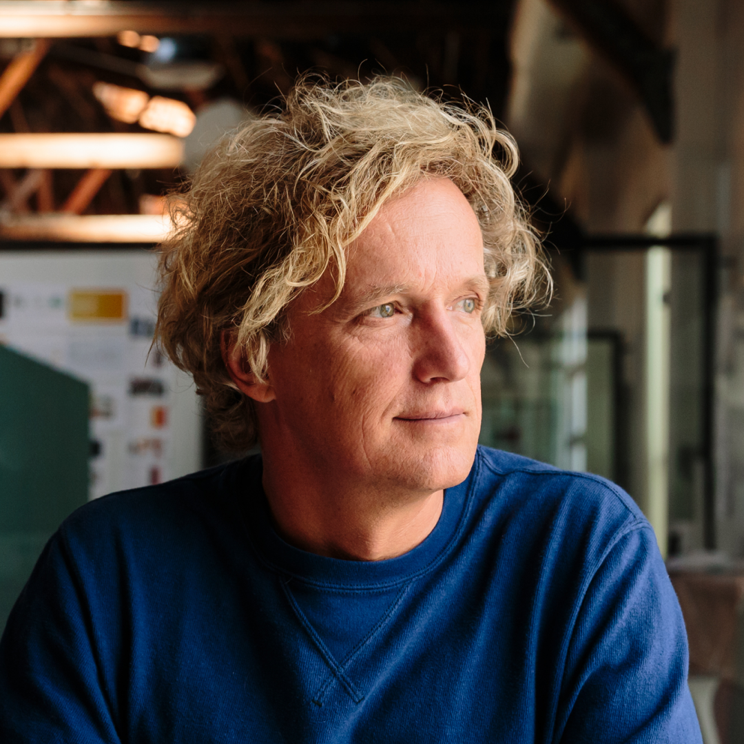 Man with curly blonde hair and beard in blue sweater