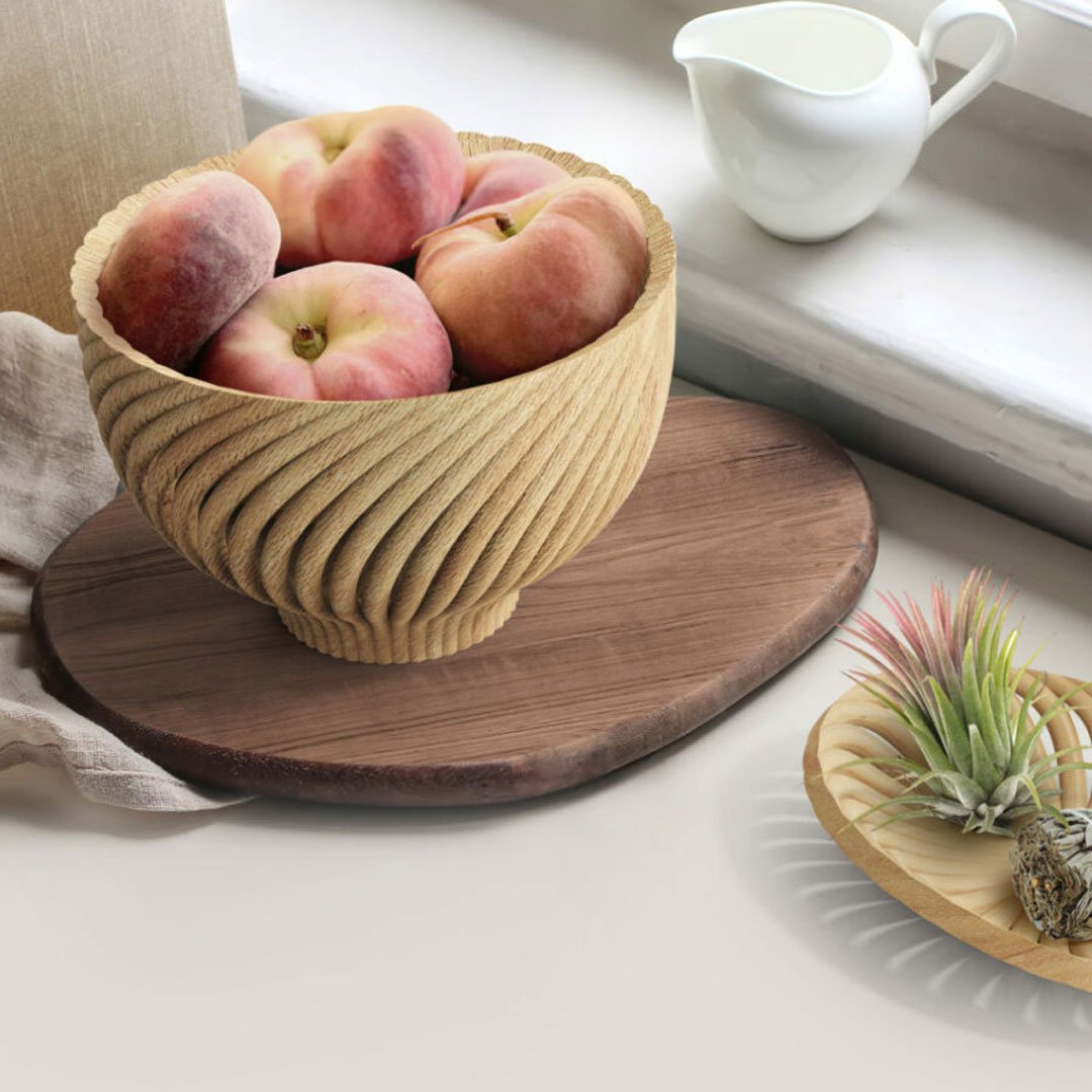 Bowl of peaches on wooden tray with wavy design next to small plant