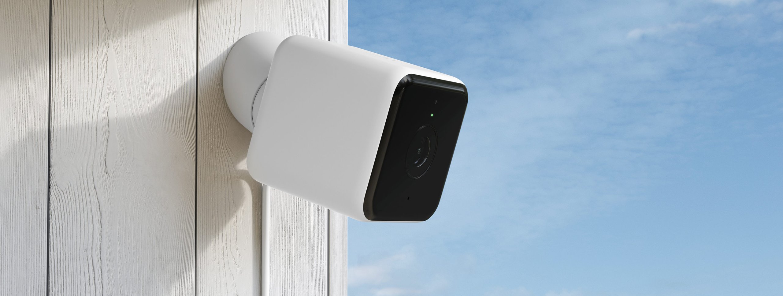 White security camera mounted on wooden surface against blue sky