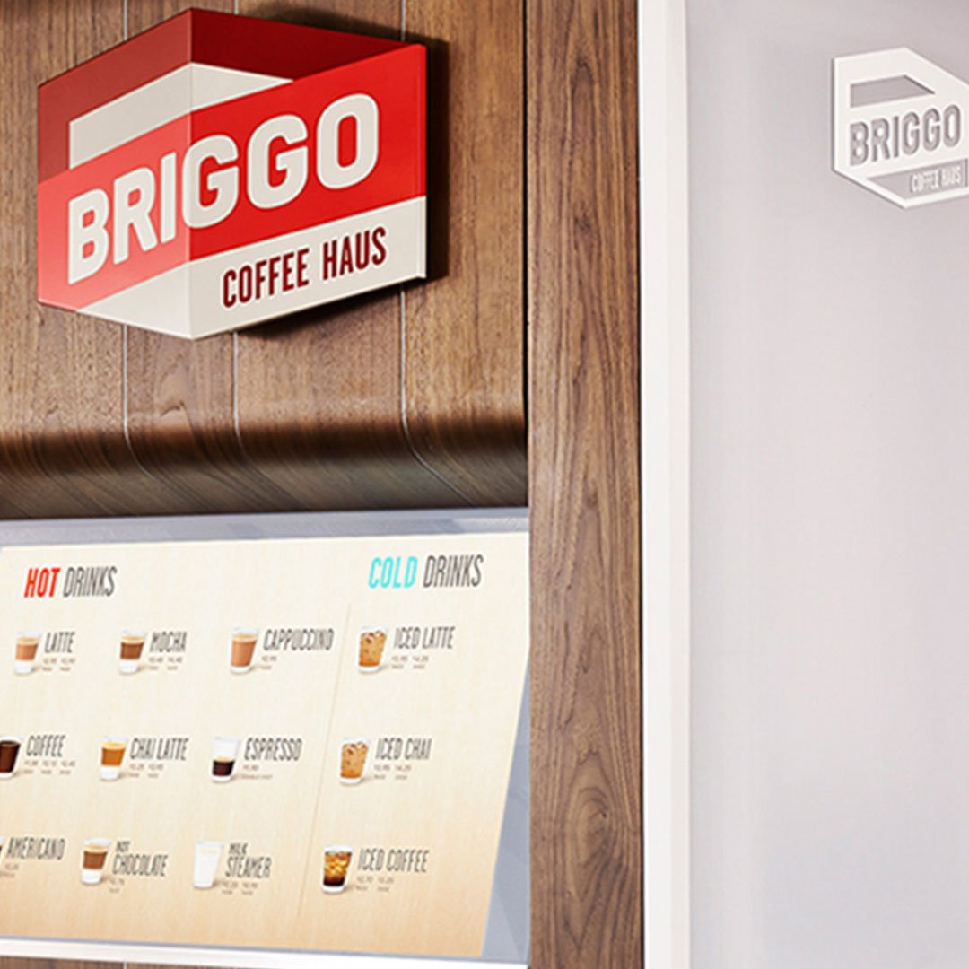 Sign for Briggo Coffee Haus in front of a wooden wall with menu board