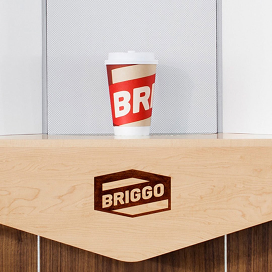 Red and white BRIGO logo on a coffee cup with a wooden surface