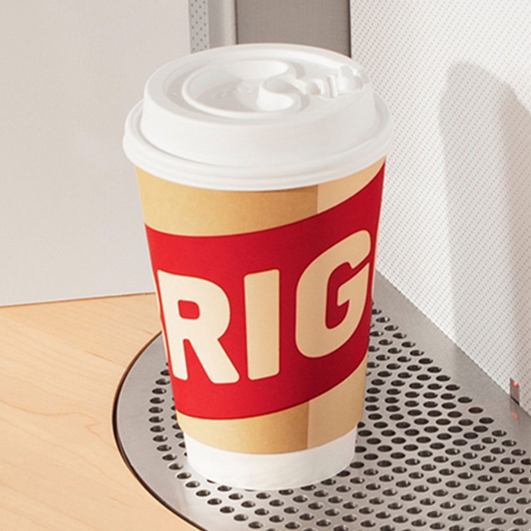 RIG-branded paper coffee cup with red and gold label on the pickup turntable of a Briggo automated coffee kiosk