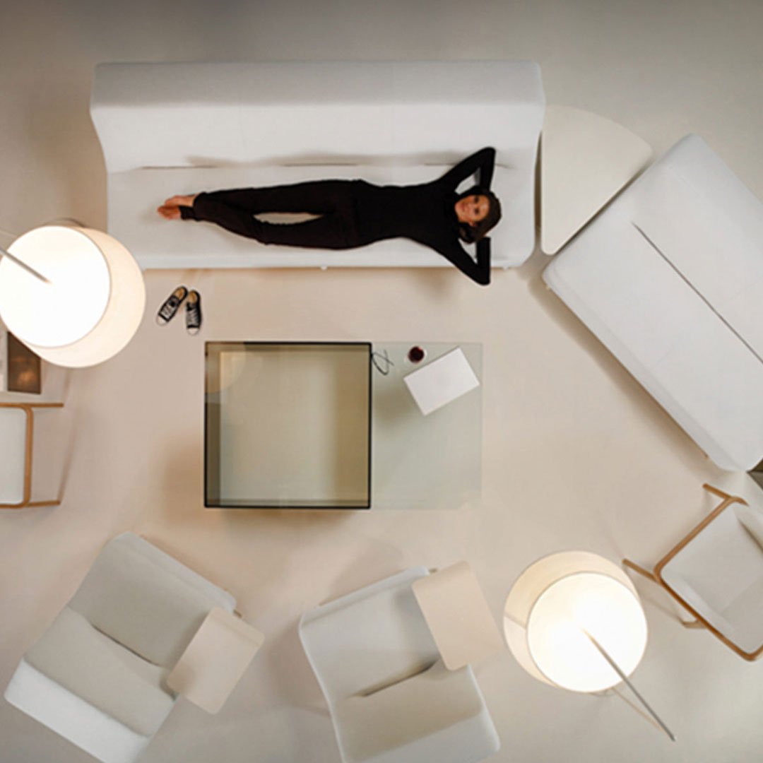 HBF woman lying on a white sofa in a bright neutral-toned living room with armchairs