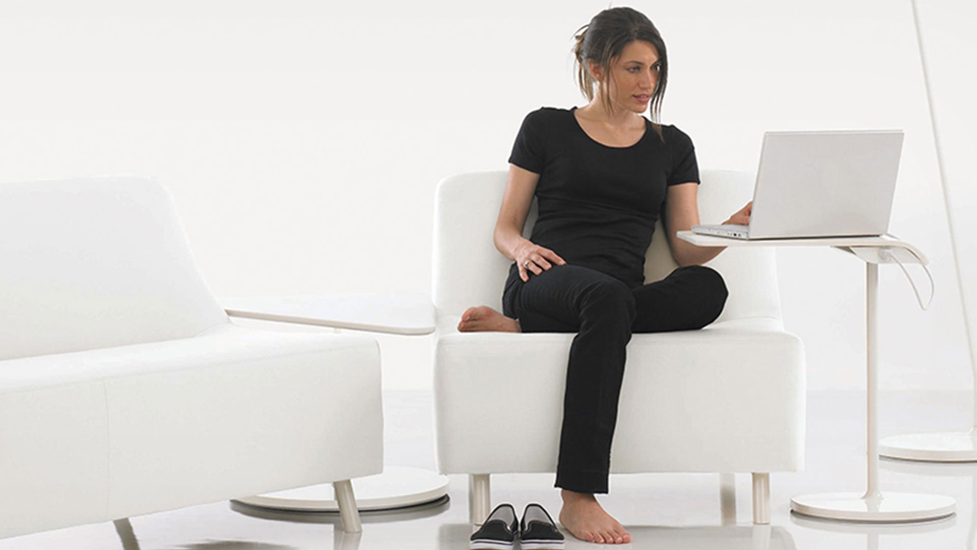 HBF woman in black working on a laptop while seated on a white couch flanked by two armchairs