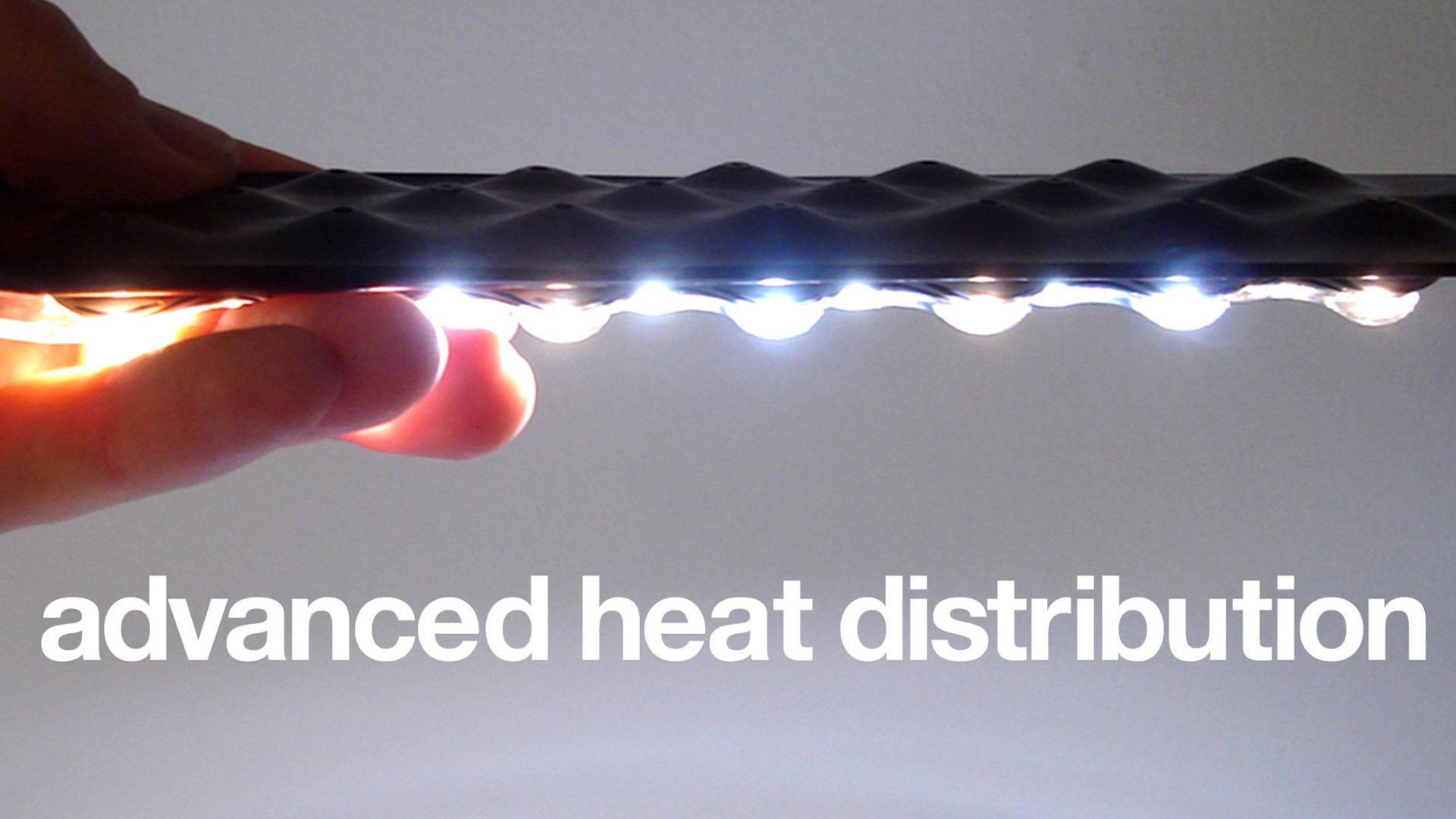 Hand holding rectangular device with light and 'ADVANCED HEAT DISTRIBUTION' text.